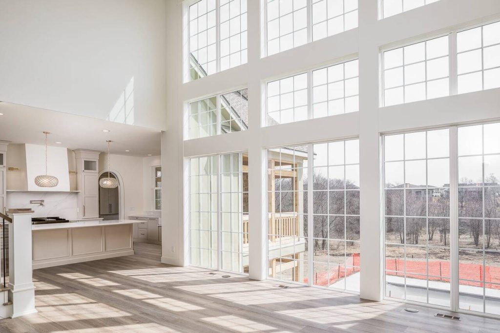 Modern, bright living space with large floor-to-ceiling windows and an open kitchen, overlooking a yard.