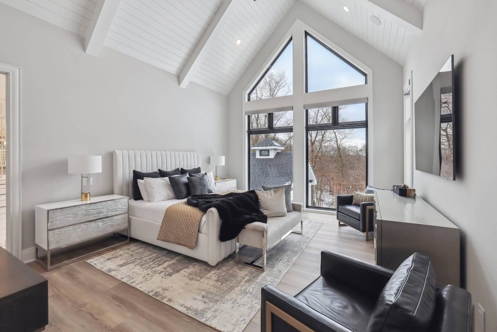 Modern bedroom with vaulted ceiling, large windows, neutral tones, and contemporary furniture.
