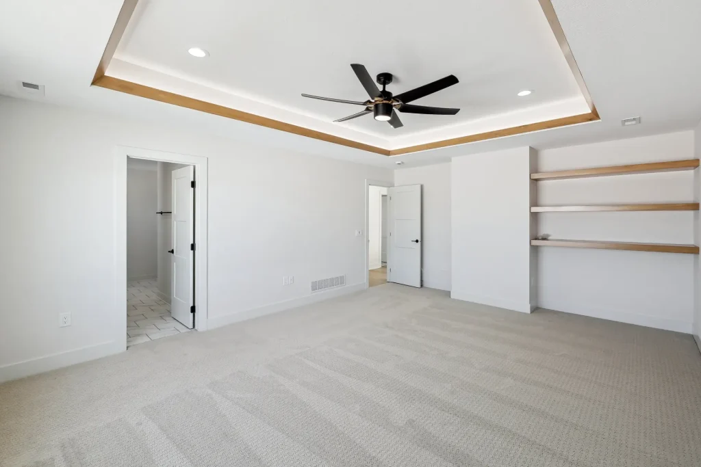 A newly built custom home bedroom with a tray ceiling, recessed lighting, and ceiling fan